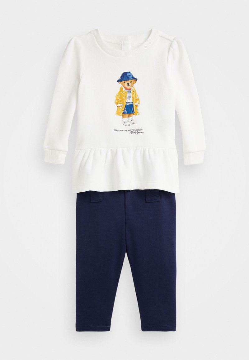 White long-sleeve top with a bear graphic in yellow raincoat and blue hat, paired with dark blue leggings featuring two pocket faux designs.