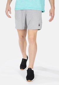 Pantalones cortos atléticos grises hechos de tejido suave con una cintura elástica y un logo lateral. Combinados con zapatillas negras con suelas blancas.