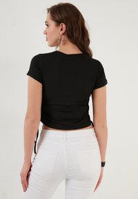 Zwarte ribbed top met korte mouwen en een aansluitend ontwerp, voorzien van een ronde halslijn en zijsplits. Gecombineerd met witte hoge taille jeans.