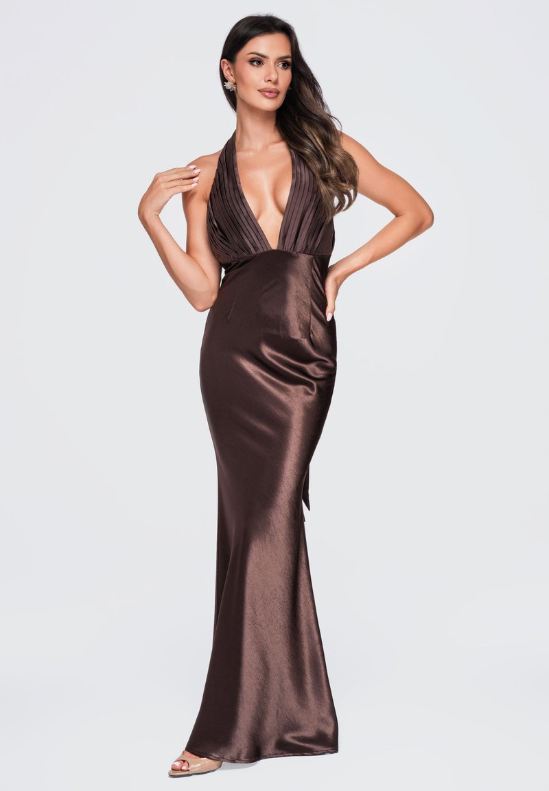 Femme aux longs cheveux foncés portant une robe de soirée en satin marron foncé avec un col halter, posant sur un fond clair uni.
