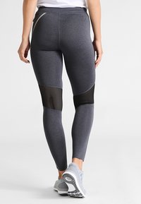 Szare legginsy sportowe z elastycznego materiału o dopasowanym kroju. Posiadają siateczkowe wstawki na łydkach oraz odblaskowy akcent w pasie.