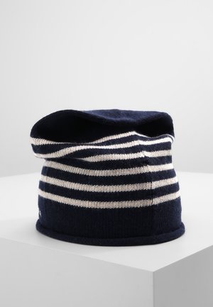 Marineblauwe en witte gestreepte gebreide muts met een losse pasvorm, tentoongesteld op een wit voetstuk tegen een effen achtergrond.