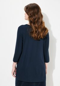 Laivansinis pitkähihaine paita pyöreällä kaula-aukolla. Pehmeää materiaalia, rento malli ja hieman pidempi helma takana. Ei näkyviä kuvioita tai yksityiskohtia.