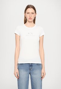 T-shirt bianca a maniche corte, colletto rotondo, con un logo argentato "A|X ARMANI EXCHANGE" al centro. Tessuto di cotone liscio.