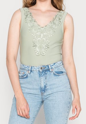 Lys grøn bodysuit med dyb V-udskæring, der har intrikate blomsterbroderier ved udskæringen; parret med lyseblå højtaljede jeans.