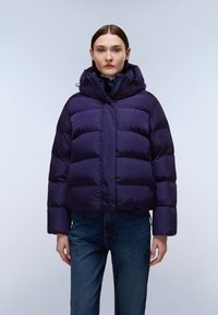 Fioletowa kurtka puchowa z krótkim krojem, posiadająca kaptur, pikowaną fakturę oraz elastyczne akcenty przy mankietach, zestawiona z dżinsami.
