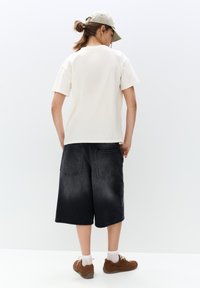 Beige bomulds T-shirt med klassisk pasform, parret med sorte denimshorts med to baglommer og en falmet tekstur. Brune sneakers fuldender looket.