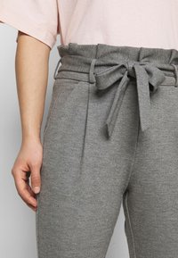 Szare dresy z teksturą materiału, z wiązanym paskiem w talii i kieszeniami bocznymi. Odzież zestawiona jest z jasnoróżową bluzką.