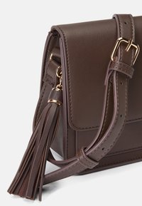 Brun lær crossbody-veske med klaffelukking, gullfarge detaljer og en duskdetalj på stroppen. Teksturert overflate og strukturert design.