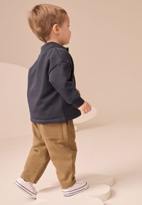 Tengerészkék pulóver laza szabással, bézs nadrággal, amelyen hátul zsebek találhatók, valamint fehér tornacipőkkel piros csíkokkal. Összességében egyszerű kialakítás.