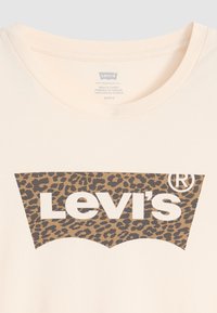 Kreminės spalvos marškinėliai su leopardų rašto Levi's logotipu rudos spalvos, apvaliu kaklu ir minkšta medvilnės tekstūra.
