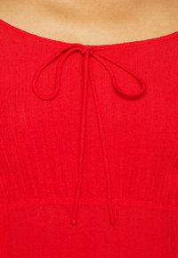 Červené šněrovací šaty z jemně vroubkované tkaniny, s kulatým výstřihem a stahovací šňůrkou uprostřed, hladkou texturou a přiléhavým tělem.