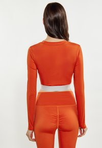 Oranje cropped longsleeve top met een witte tailleband, gecombineerd met bijpassende high-waisted leggings met een geplooid detail aan de achterkant.