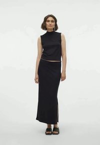 Black sleeveless top paired with a matching long skirt featuring side slits, made from smooth fabric, with a fitted silhouette. Black sandals.