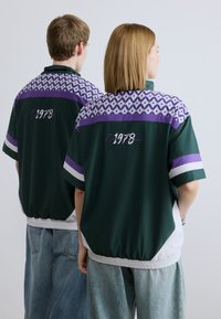 Πράσινο πουκάμισο κοντομάνικο με μοβ και μοτίβο στο ντεκολτέ. Διαθέτει ελαστικό τελείωμα και κεντημένο "1978" στην πλάτη. Άνετη εφαρμογή και υφή υφάσματος.