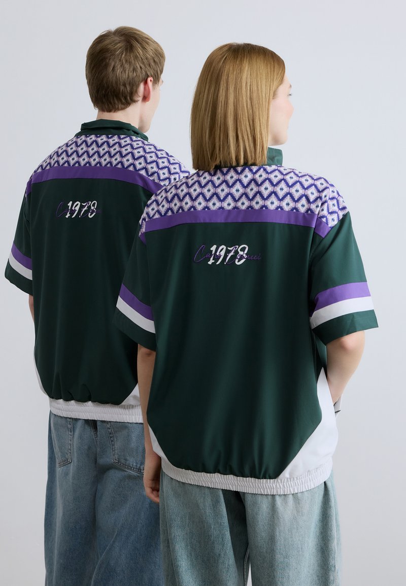 Πράσινο πουκάμισο κοντομάνικο με μοβ και μοτίβο στο ντεκολτέ. Διαθέτει ελαστικό τελείωμα και κεντημένο "1978" στην πλάτη. Άνετη εφαρμογή και υφή υφάσματος.