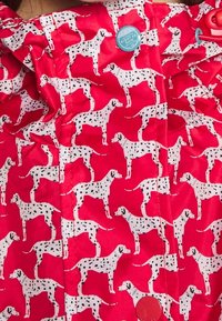 Czerwony materiał z powtarzającym się wzorem białych psów dalmatyńskich z czarnymi plamami; zawiera niebieski guzik na przodzie.