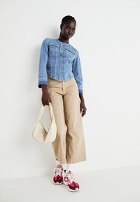Jeans jakna s gumbom, svetlo modre barve; bež široke hlače; rdeče in roza superge; off-white torba čez ramo.
