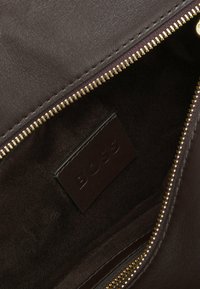 Tummanruskean nahkalaukun sisäpuoli, jossa on kultainen vetoketju ja ommeltu nahkalappu, johon on painettu "BOSS".