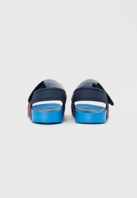Granatowe klapki na suwak o matowym wykończeniu, z niebiesko-czerwoną podeszwą, regulowanym paskiem i otwartym tyłem dla łatwego zakładania.