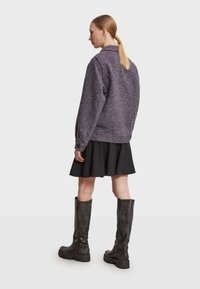 Lilla struktureret jakke med høj krave, parret med en sort udskåret nederdel og knæhøje sorte læderstøvler.