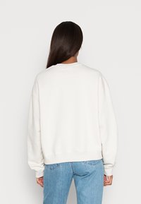 Sweatshirt branco com decote redondo e mangas longas, apresentando punhos e barra canelados. O tecido parece suave e ligeiramente elástico.