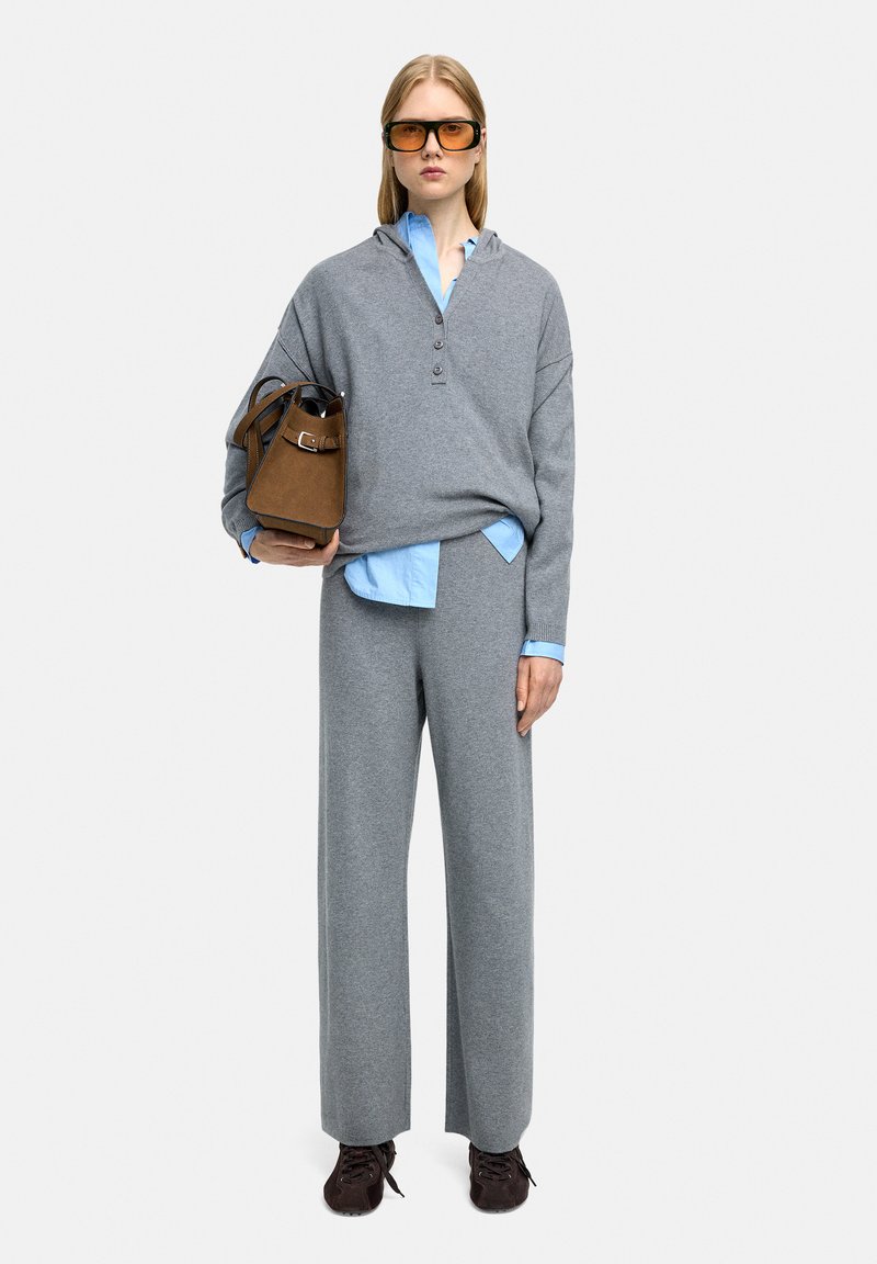 Szary, oversize'owy hoodie z trzema guzikami, zestawiony z jasnoniebieską koszulą z kołnierzykiem i szerokimi szarymi spodniami. Brązowa torebka i ciemne buty.