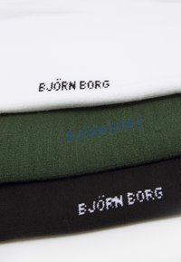 Drei übereinander gestapelte Kopfbänder aus Baumwollfrottee: weiß, grün und schwarz, jeweils mit gesticktem "EJÖRN BORG"-Logo in kontrastierenden Farben.