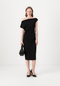 Juodas off-shoulder midi suknelė iš elastingos medžiagos, turinti drapiruotę, prigludusią siluetą ir subtilų raukšlėjimą iš vienos pusės. Juodas rankinukas kaip akcentas.