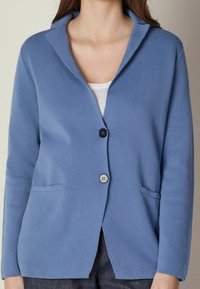 Ljusblå stickad cardigan med amerikansk krage, enkel knappstängning, två fickor och ett strukturerat tyg.