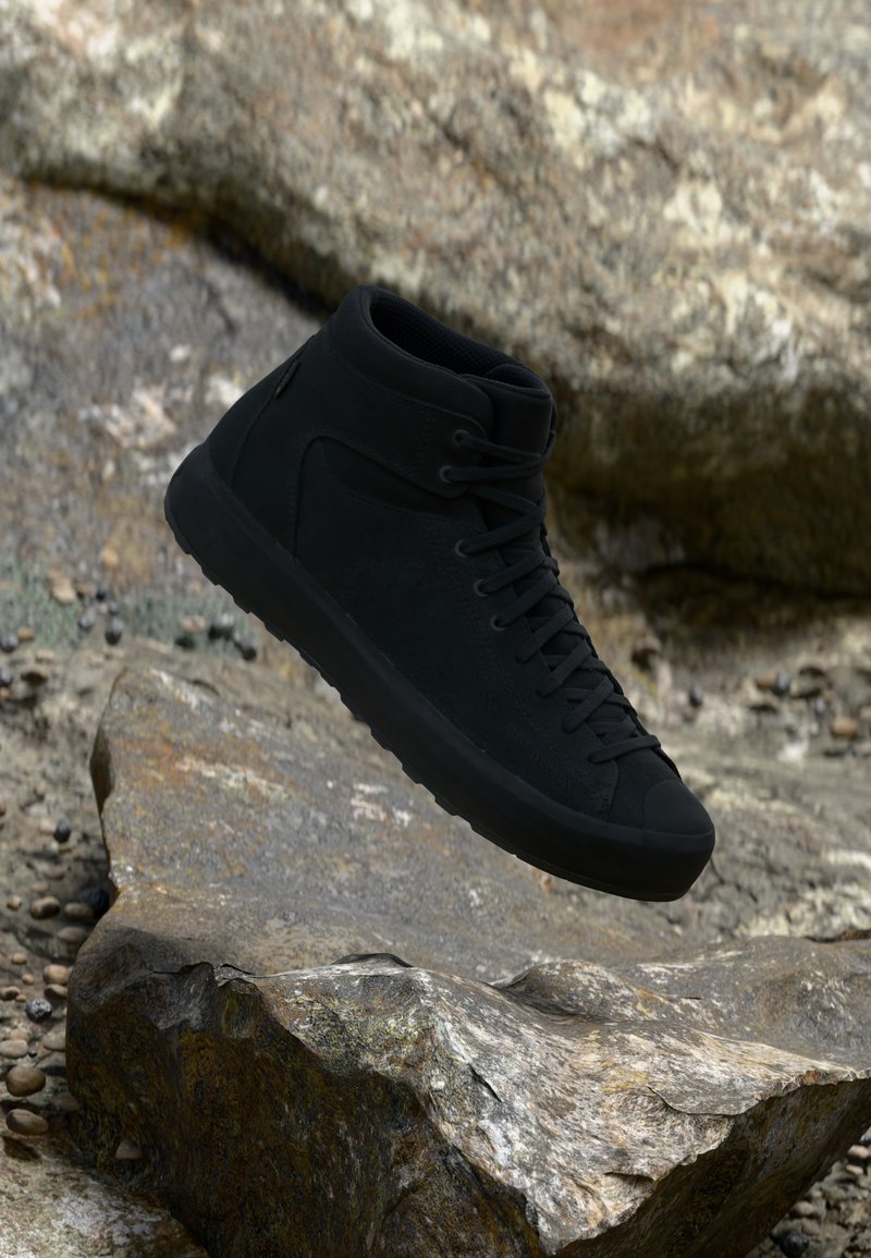 Shoe de cano alto preto com parte superior em camurça, design de atacadores e sola de borracha. Apresenta um acabamento texturizado e uma silhueta aerodinâmica.