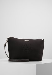 Pochette noire à fermeture éclair avec motif floral en relief et bandoulière amovible, présentée sur une surface blanche avec un fond uni.