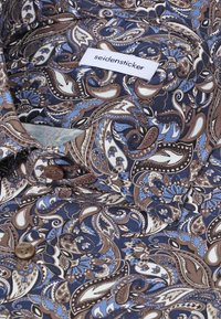 Chemise pliée avec motif paisley marron et bleu, boutons marron, et étiquette blanche avec l'inscription "seidensticker" sur le col.
