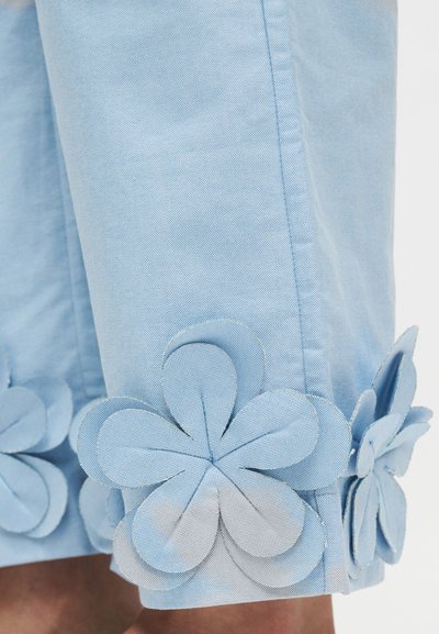 Pantaloni scurți din material albastru deschis, cu aplicații mari în formă de flori în aceeași nuanță de albastru, cu design stratificat de petale la tivul inferior.