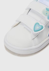 Hvitt lær sneakers med rund tå, to borrelåsremmer, og dekorative blå hjerte- og skydetaljer på siden.