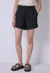 Pantaloni corti neri in lino con vita elastica, tasche laterali e vestibilità comoda. Abbinati a sandali neri chunky con dettagli in metallo.
