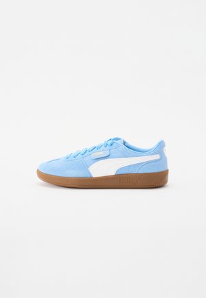 Lichtblauwe Puma suède sneaker met wit streepdetail en bruine rubberen zool, zijaanzicht op witte achtergrond.