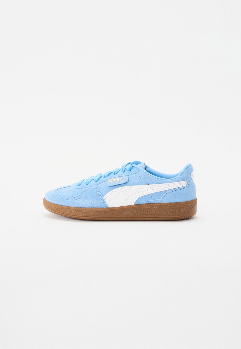 Sneaker en daim Puma bleu clair avec détail de bande blanche et semelle en caoutchouc marron, présenté en profil sur fond blanc.