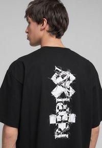 T-shirt nera con vestibilità ampia, caratterizzata da un design grafico astratto bianco sul retro. Maniche corte e scollo rotondo.