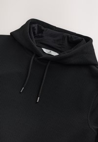 Felpa nera a coste con interno foderato. Presenta un cappuccio con coulisse e punte metalliche. Design semplice per un abbigliamento casual.