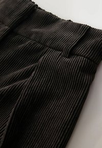 Primer plano de pantalones de pana marrón oscuro que muestran la cinturilla y la textura de los ribetes verticales en la tela.