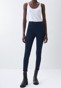 Marinblå högmidjade skinny jeans i denim med en slät yta och minimala sömnadsdetaljer. Kombineras med en vit linne och svarta ankelskor.