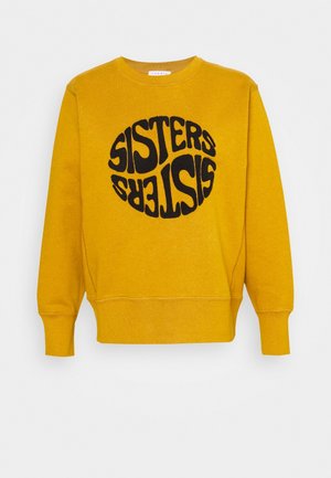 Żółta bluza z ribbowanymi mankietami i dołem, z dużym czarnym okrągłym napisem "SISTERS" w stylizowanej czcionce.