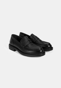Zwarte leren loafers met een gestructureerd oppervlak, ronde neus en een gestikte accenten. Dikke zwarte zool met een lichte hak, met een klassiek ontwerp.