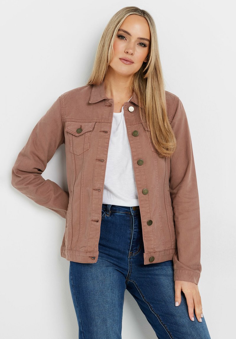 Veste en denim brun clair avec une finition texturée, deux poches poitrine, des boutons en métal et un col classique, associée à un t-shirt blanc et un jean bleu.
