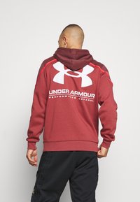 Roten Kapuzenpullover mit großem weißen Under Armour-Logo auf dem Rücken, ausgestattet mit kontrastierenden Nähten und einer strukturierten Kapuze.