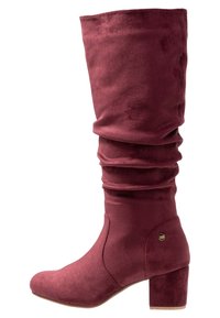 Botte en suède bordeaux, hauteur genou, au design ample, avec un bout arrondi et un talon bloc. Présente un petit logo sur le côté.