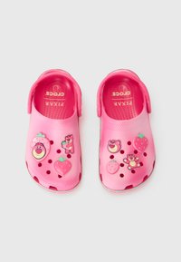 Roze Crocs s dizajnom crtića medvjeda i jagoda, izrađeni od laganog materijala, s ventilacijskim otvorima i trakama za lakše obuvanje.