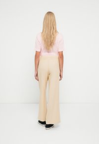 Šviesiai rožinė tekstūruota palaidinė su trumpomis rankovėmis, derinama su smėlio spalvos plataus kirpimo kelnėmis ir juodais sportbačiais, matoma iš nugaros.