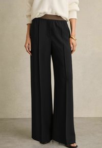 Pantaloni neri a gamba larga con un alto elastico in vita e tasche laterali discrete, realizzati in tessuto liscio e leggero.